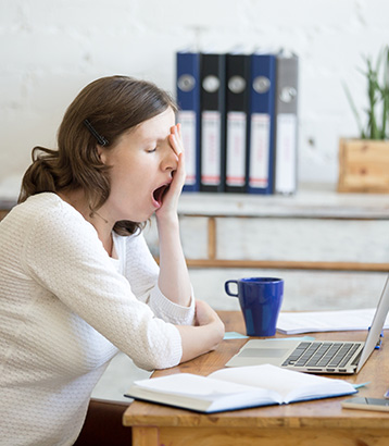 Young woman yawning in front of laptop